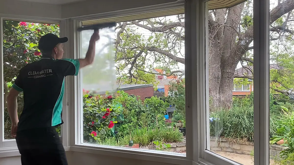 Cleaner working a squeegee across interior glass in a bay window