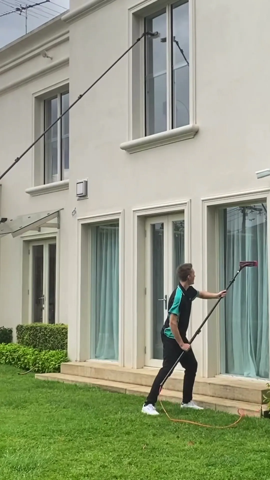 Cleaner reaching an upper-storey window from ground level with an extended water-fed pole